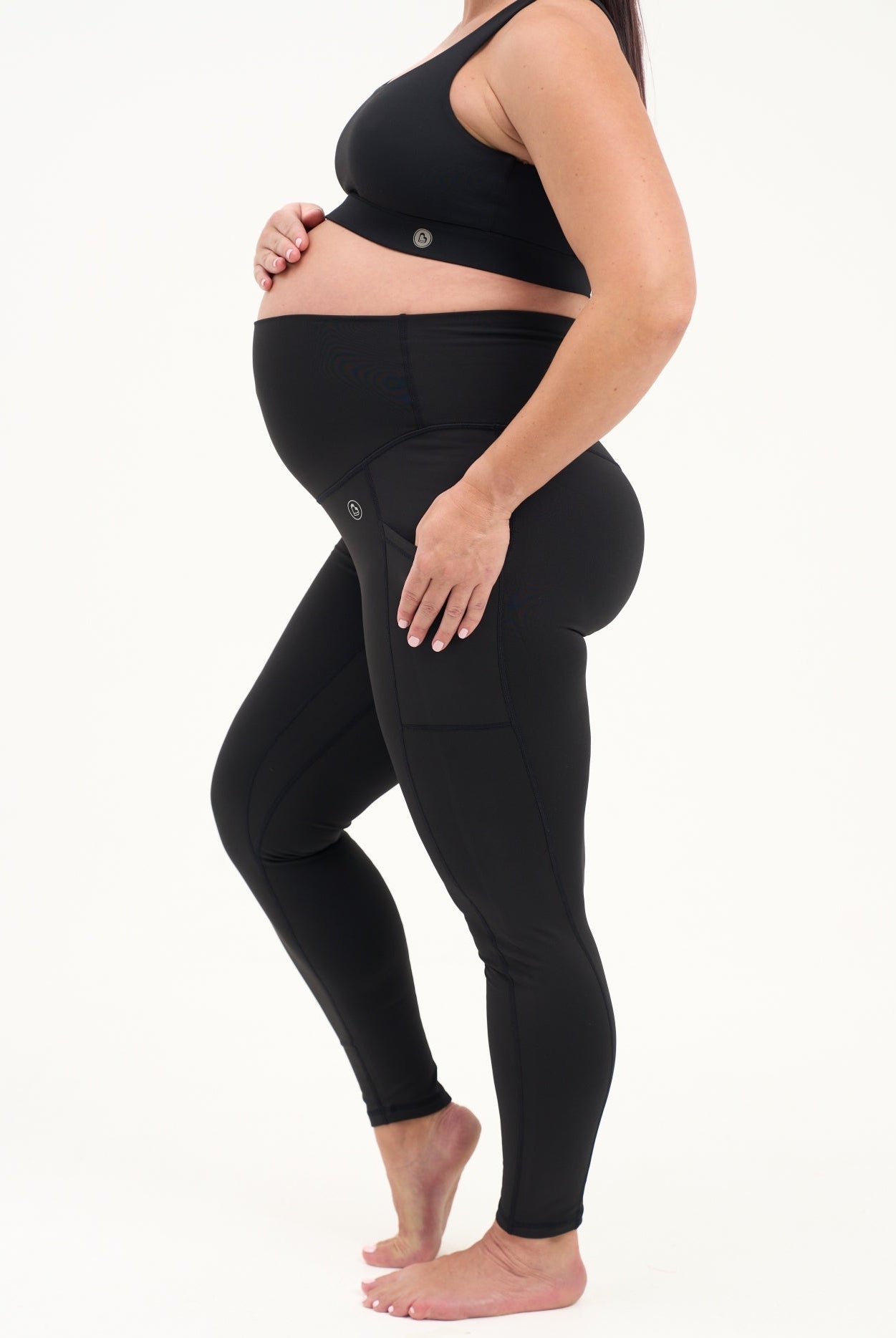 Mum wearing black maternity leggings with pockets on a white background