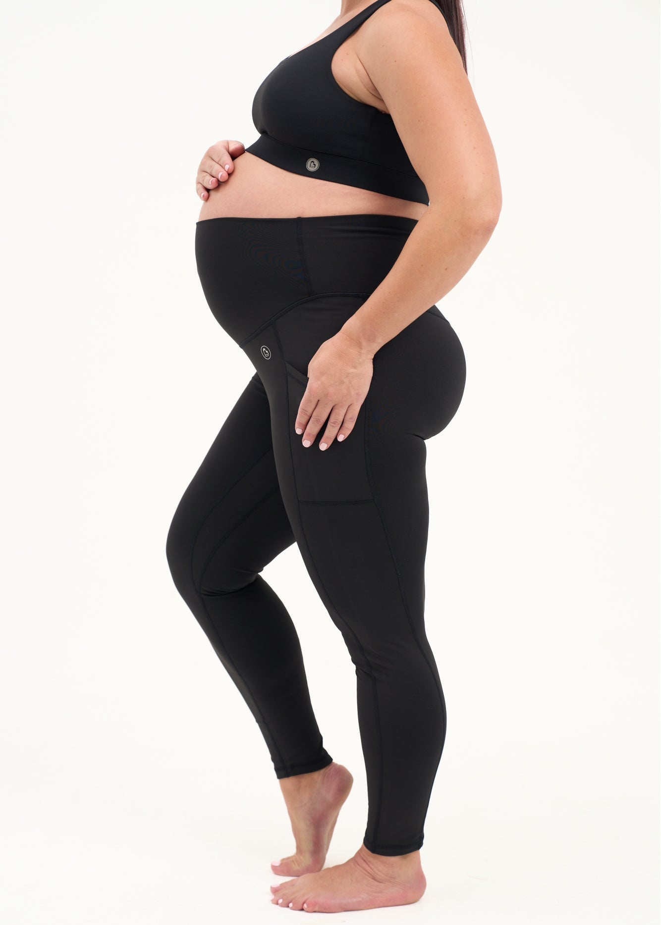 Mum wearing black maternity leggings with pockets on a white background