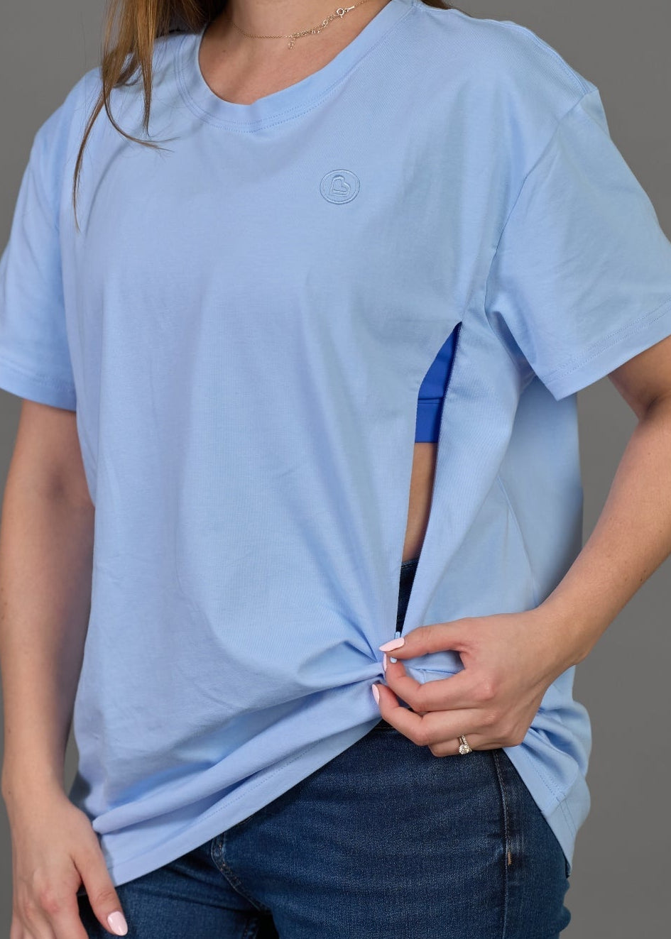 Woman wearing a light blue t-shirt and dark blue jeans against a gray background